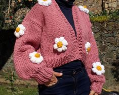 a woman wearing a pink cardigan with white flowers on the front and back buttons