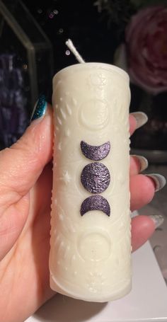 a hand holding a white candle with purple designs on it