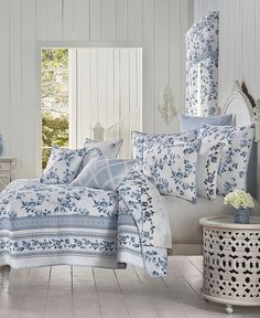 a bedroom with blue and white bedding, dressers, mirror and vase on the floor