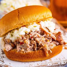 a pulled pork sandwich with cole slaw on a plate next to a glass of beer