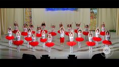 a group of children in red and white outfits on stage with their hands up to the sky