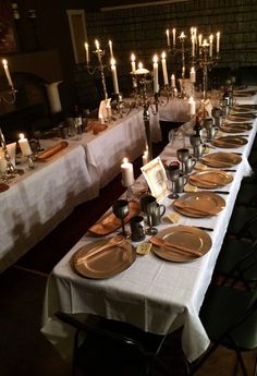 a long table is set with plates and silverware, lit by candlelight candles