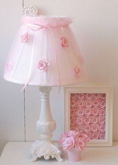 a pink lamp shade sitting on top of a white table next to a framed picture