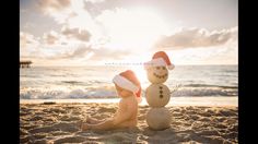 a baby sitting in the sand next to a snowman wearing a santa claus hat