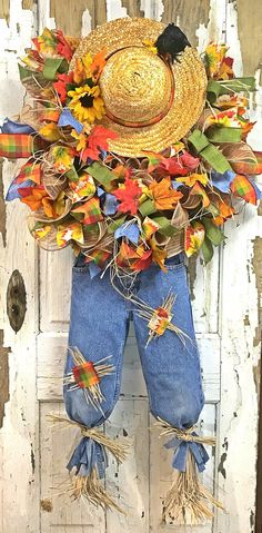 a scarecrow door hanger decorated with fall leaves and a straw hat on it