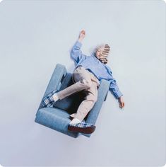 a man laying on top of a blue couch with his arms up in the air