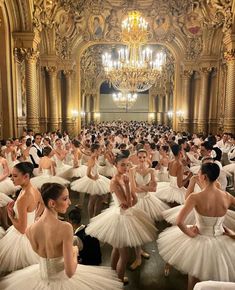 a large group of ballerinas in white tutus and dresses with chandeliers hanging from the ceiling