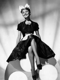 a black and white photo of a woman in a dress sitting on a large object