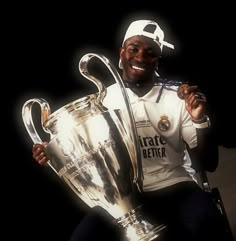 a man sitting in front of a trophy holding a soccer ball and wearing a white hat