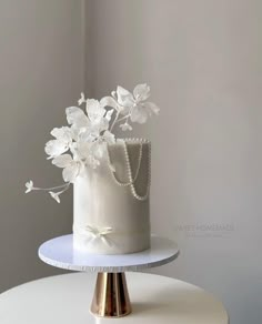 a white wedding cake with flowers on the top and pearls in the middle is sitting on a table