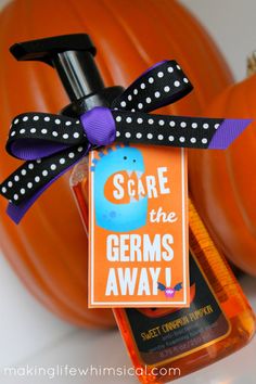 an orange bottle with a purple ribbon and some black polka dots on it, sitting next to a pumpkin