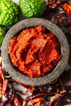 a small bowl filled with red sauce next to some green and orange vegetables on a table