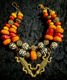 African inspired Tribal jewelry has never looked SO HOT! This double stranded ethnic statement necklace features Moroccan resin, lost wax brass cage work beads, batik zebu bone beads, wood rondelles, vintage brass beads, red branch coral nuggets and other gold tone metals. Adjusting from 17-19", this has a gold tone hook closure and a 2"extender chain which I can lengthen if requested. A very rare double Crocodile or Alligator brass pendant is the focal point and measures 5" x 4.5". A stunning piece worn with a tan or on women of color! From the Atelier of Kat Kouture! Unique Double Strand Beaded Necklaces, Unique Double Strand Beaded Necklace, Traditional Handmade Double Strand Beaded Necklace, Traditional Handmade Double Strand Beaded Necklaces, Traditional Double Strand Beaded Jewelry, Unique Handmade Double Strand Beaded Necklaces, Handmade Unique Double Strand Beaded Necklaces, Traditional Brass Jewelry With Colorful Beads, Unique Hand-strung Necklaces For Rituals