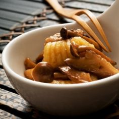 a bowl filled with bananas and nuts on top of a wooden table next to a spoon