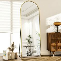 a large mirror sitting on top of a wooden floor next to a dresser and lamp