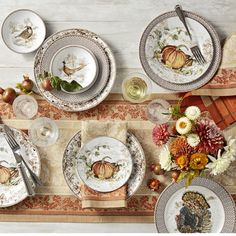 the table is set for thanksgiving dinner with plates and silverware, pumpkins and flowers