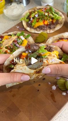 a person is holding a pita sandwich in front of some other food on a cutting board