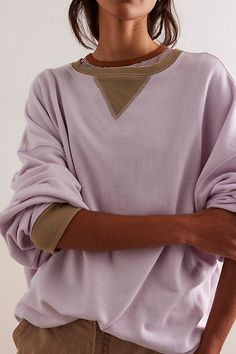 a woman wearing a purple sweater and khaki pants with her arms folded over her chest