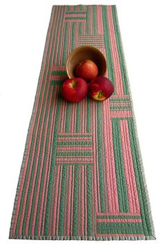 two apples are sitting in a bowl on a table runner with pink and green stripes