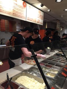 some people are preparing food at a buffet line in a fast food restaurant with menus on the wall behind them