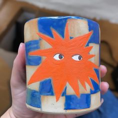 a hand holding a ceramic cup with an orange star painted on the side and eyes