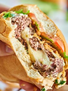 a close up of a person holding a sandwich with meat and veggies on it