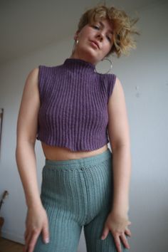 a woman with her hands on her hips wearing green pants and a purple crop top