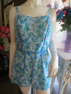 -style 1950s' floral one-piece romper style swimsuit by Perfection Fit/Rosanne, in a size 18/40.  Swimsuit has back metal zipper closure, skinny tie belt, small adjustable buttoned shoulder straps, slight pointy bust, blue front bodice trim, stretchy sides in the bodice backs, and fabric is cotton/Dacron/polyester. Swimsuit leg bottom has elastic under pants. Floral cotton fabric print is different sizes of daises in colors of teal, light green, white, and light blue.  Swimsuit is in good condition, but no padding in bra/bust area. WAIST=32-34"   BUST=36-38"/B cup   HIP=40-42"   THIGH=26-30"    PRICE IS $45.00-----SALE FINAL/AS IS/NO RETURNS. Vintage Floral Print Jumpsuits And Rompers, Retro Sleeveless Floral Print Jumpsuits, Retro Floral Print Sleeveless Jumpsuits, Retro Summer Floral Jumpsuits And Rompers, Retro Floral Print Fitted Jumpsuits And Rompers, Retro Sleeveless Floral Jumpsuits And Rompers, Retro Fitted Floral Print Jumpsuits And Rompers, Vintage Floral Print Jumpsuit For Spring, Fitted Vintage Floral Print Jumpsuits And Rompers