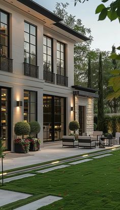 a large white house with lots of windows and plants in the front yard at dusk