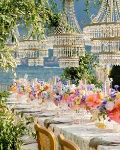 an outdoor dining area with chandeliers and flowers on the table, surrounded by greenery