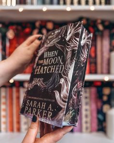 a person holding up a book in front of a bookshelf