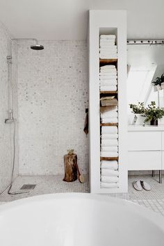 the bathroom is decorated in white and has lots of towels on shelves above the shower