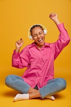 a woman sitting on the floor with headphones in her ears and wearing pink shirt