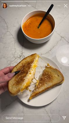 a person is holding a grilled cheese sandwich over a bowl of soup