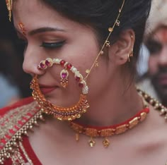 a woman wearing an elaborate necklace and nose ring with jewelry on her face, looking down at the ground