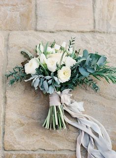 a bouquet of white roses and greenery on a stone wall with ribbon tied around it