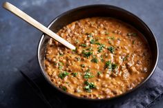 a bowl filled with beans and parsley on top of a napkin next to a wooden spoon