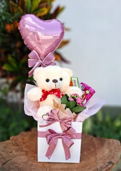 a teddy bear sitting in a gift box with flowers and heart shaped balloon on top