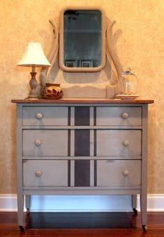 a dresser with a mirror and lamp on top of it in front of a wall