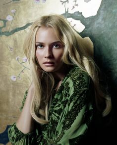 a woman with long blonde hair sitting in front of a wall and looking at the camera