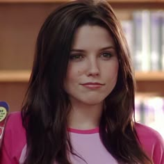 a close up of a person wearing a pink shirt and holding a toothbrush in her hand