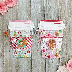 two coffee cups decorated with gingerbreads and candy canes are sitting next to pink flowers