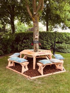 a wooden table and bench under a tree in the grass with blue cushions on it