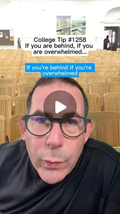 a man with glasses and a black shirt in front of rows of wooden chairs is looking at the camera