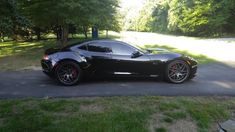 a black sports car is parked on the side of the road in front of some trees