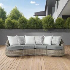 an outdoor couch with many pillows on top of it in the middle of a wooden deck