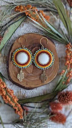 a pair of earrings sitting on top of a piece of wood next to pine cones