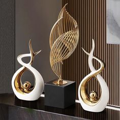 three decorative sculptures on a shelf in a room with striped walls and flooring, one is gold and the other is white