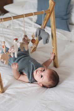 a baby laying on its back in front of a wooden frame with stuffed animals hanging from it