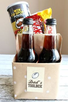 two bottles of soda sit in a box on a table next to some snacks and chips